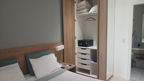 A hotel room with a bed, a bedside table, a wardrobe with a hanging organizer, and a small desk with a chair. - Premium Apartment | Pool, Kitchen and Parking Space (Rio de Janeiro)