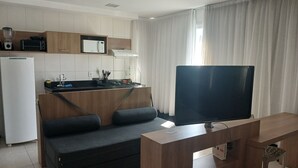 A compact living space with a kitchenette, a sofa, a TV, and a desk area. - Premium Apartment | Pool, Kitchen and Parking Space (Rio de Janeiro)