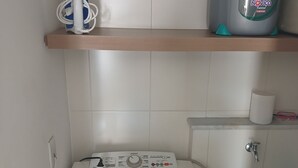 A compact laundry area with a washing machine, a drying machine, a sink, and a shelf with a kettle. - Premium Apartment | Pool, Kitchen and Parking Space (Rio de Janeiro)