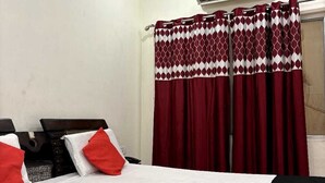 Habitación de hotel con dos camas, cortinas rojas y blancas, un aire acondicionado y un ventilador de techo.