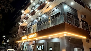 Un hotel de varios pisos con un llamativo letrero 'HOTEL SHIVAY', plantas en macetas exteriores y vehículos estacionados.