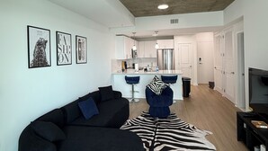 Un saló modern amb un sofà seccional negre, una catifa amb dibuixos de zebra i una cuina al fons.