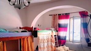Un dormitorio con literas, una escalera, una mesita pequeña y una ventana con cortinas.