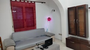Una sala de estar con un sofá, un armario, una lámpara y un ordenador portátil sobre una mesa.