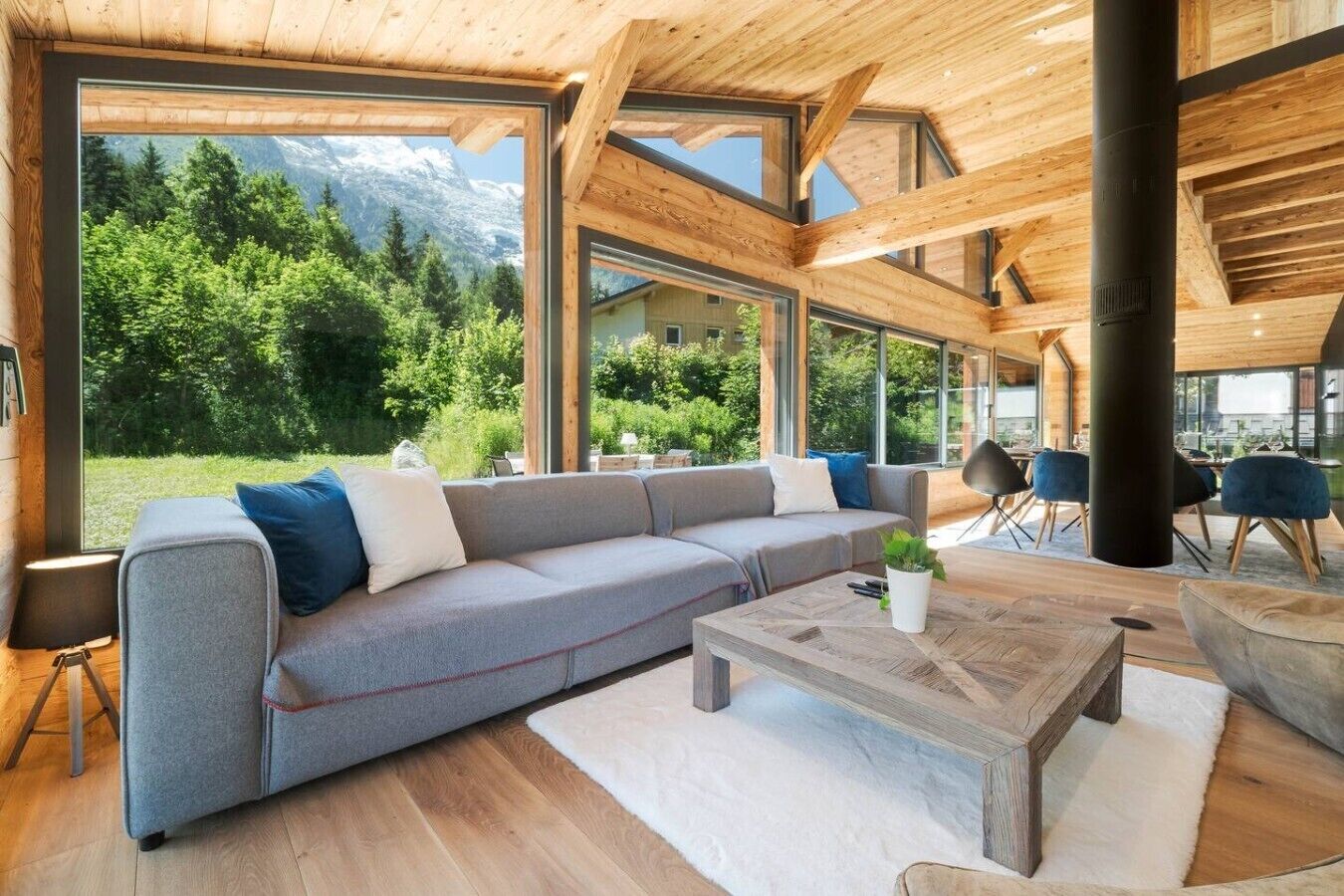 A modern interior with a large wooden ceiling, a grey sofa, and a view of a mountainous landscape.