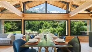 A dining area with a table set for six, large windows, and a view of a mountainous landscape. - Orion - 200 m² Chalet | 5 Bedrooms | View | Terrace & Garden (Chamonix-Mont-Blanc)