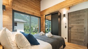 A bedroom with a large bed, wooden ceiling, and a view of the outdoors. - Orion - 200 m² Chalet | 5 Bedrooms | View | Terrace & Garden (Chamonix-Mont-Blanc)