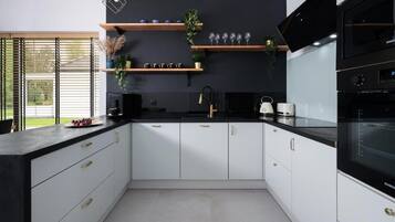 A modern kitchen with white cabinets, black countertops, and a black backsplash. There are two black ovens, a microwave, and a sink with a gold faucet.