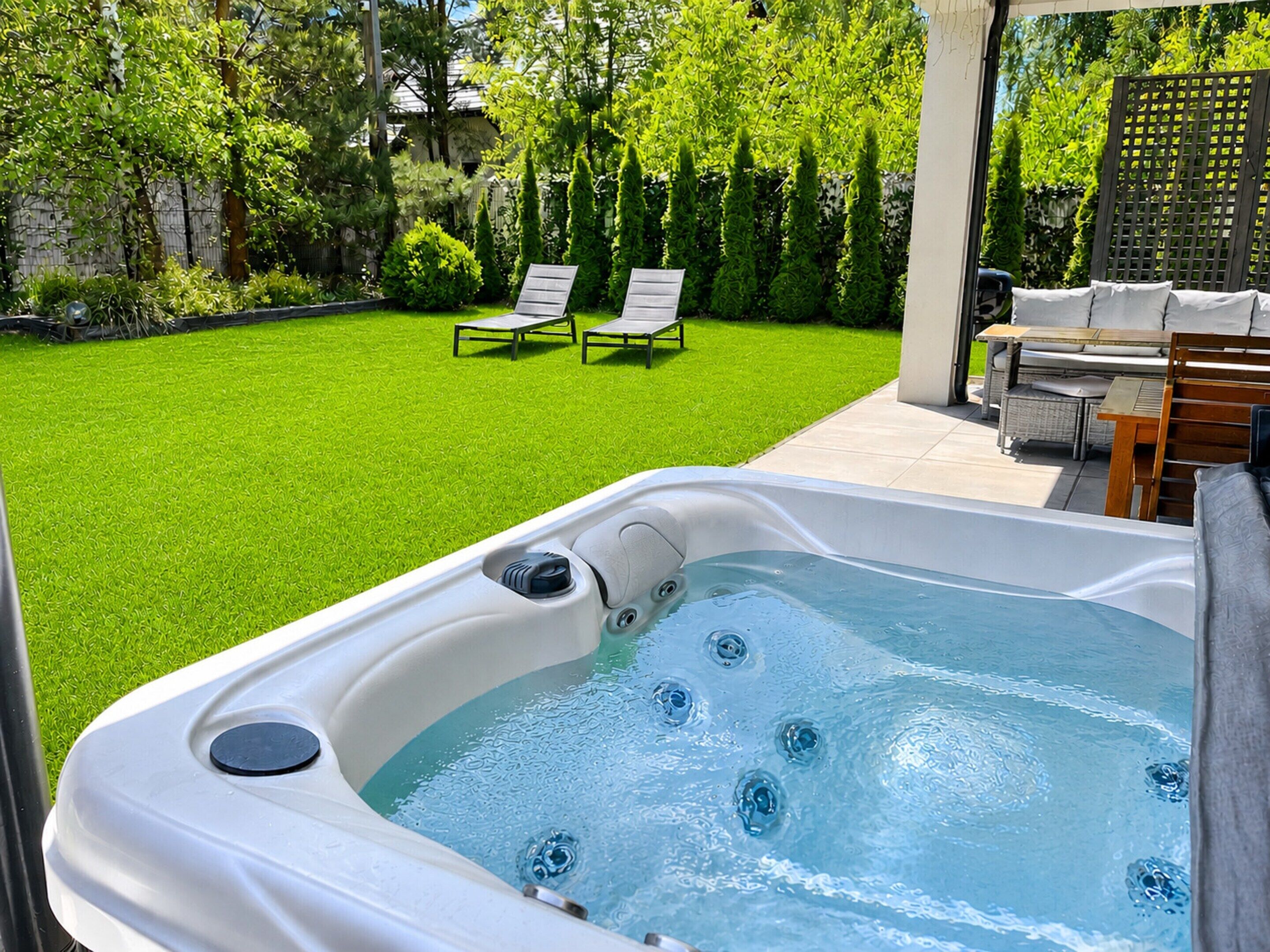 A hot tub with a grassy yard, two lounge chairs, and a wooden table.