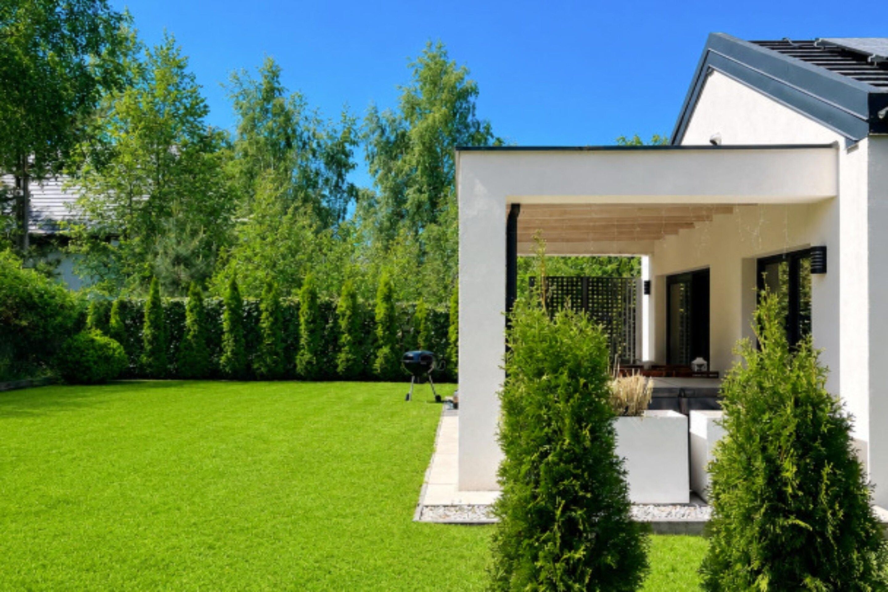 A modern house with a well-maintained lawn and a covered outdoor seating area.