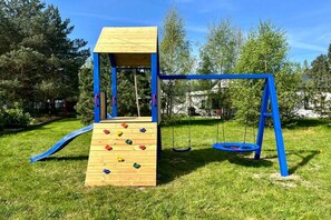 Un parque infantil con un muro de escalar de madera, columpios y un tobogán.