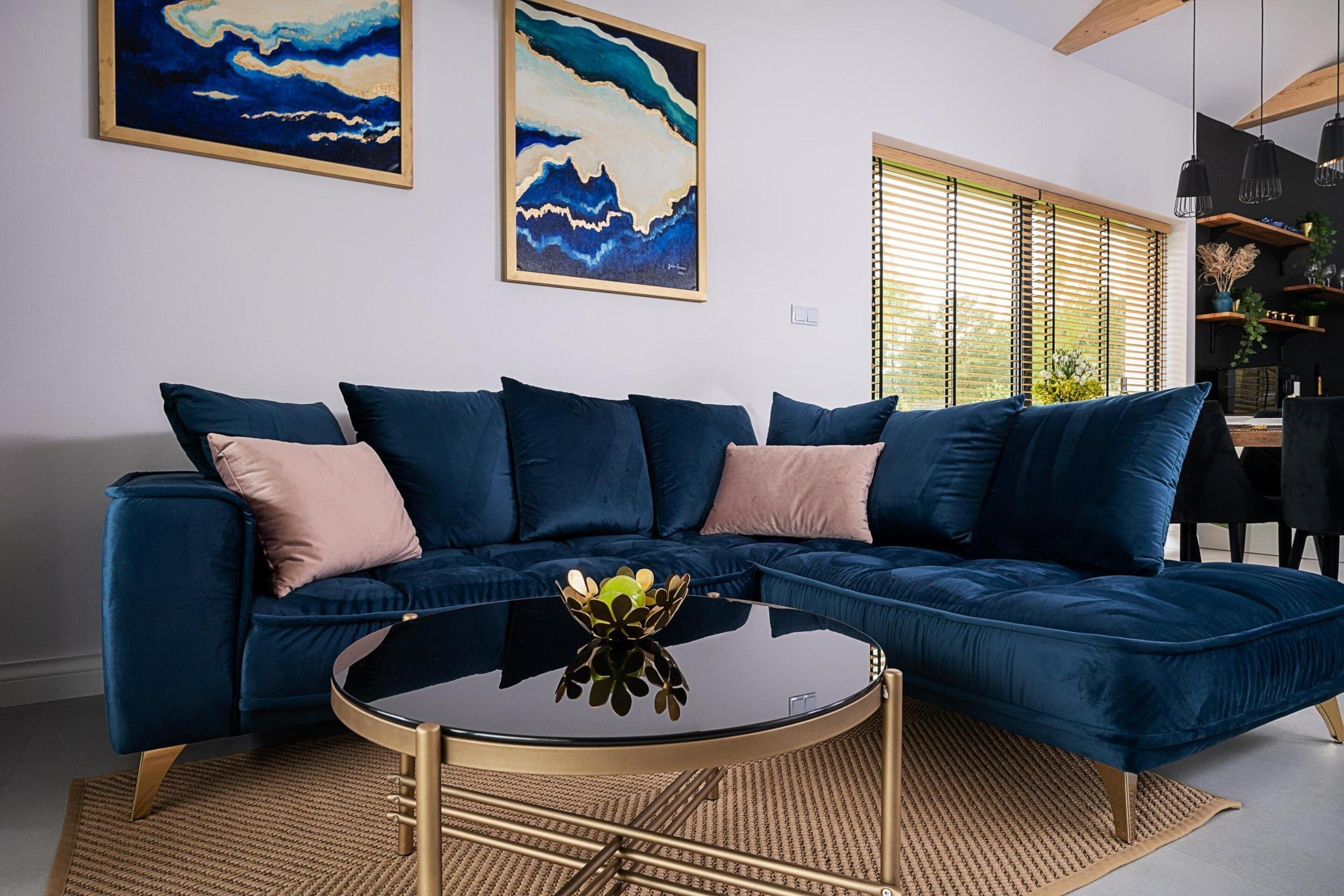 A modern living room with a dark blue sectional sofa, a round glass coffee table, and a woven rug.