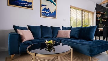A modern living room with a dark blue sectional sofa, a round glass coffee table, and a woven rug.