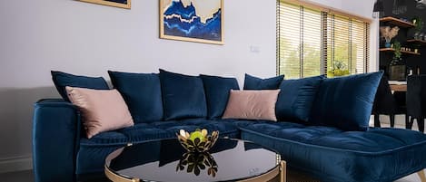 A modern living room with a dark blue sectional sofa, a round glass coffee table, and a woven rug.