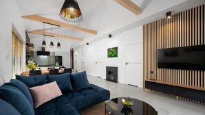 A modern living room with a sectional sofa, a fireplace, a flat-screen TV, and a dining area with a kitchen in the background. - Comfortable Holiday Home, Pool, Sauna, Jacuzzi (Krokowa)
