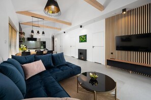 A modern living room with a sectional sofa, a fireplace, a flat-screen TV, and a dining area with a kitchen in the background. - Comfortable Holiday Home, Pool, Sauna, Jacuzzi (Krokowa)
