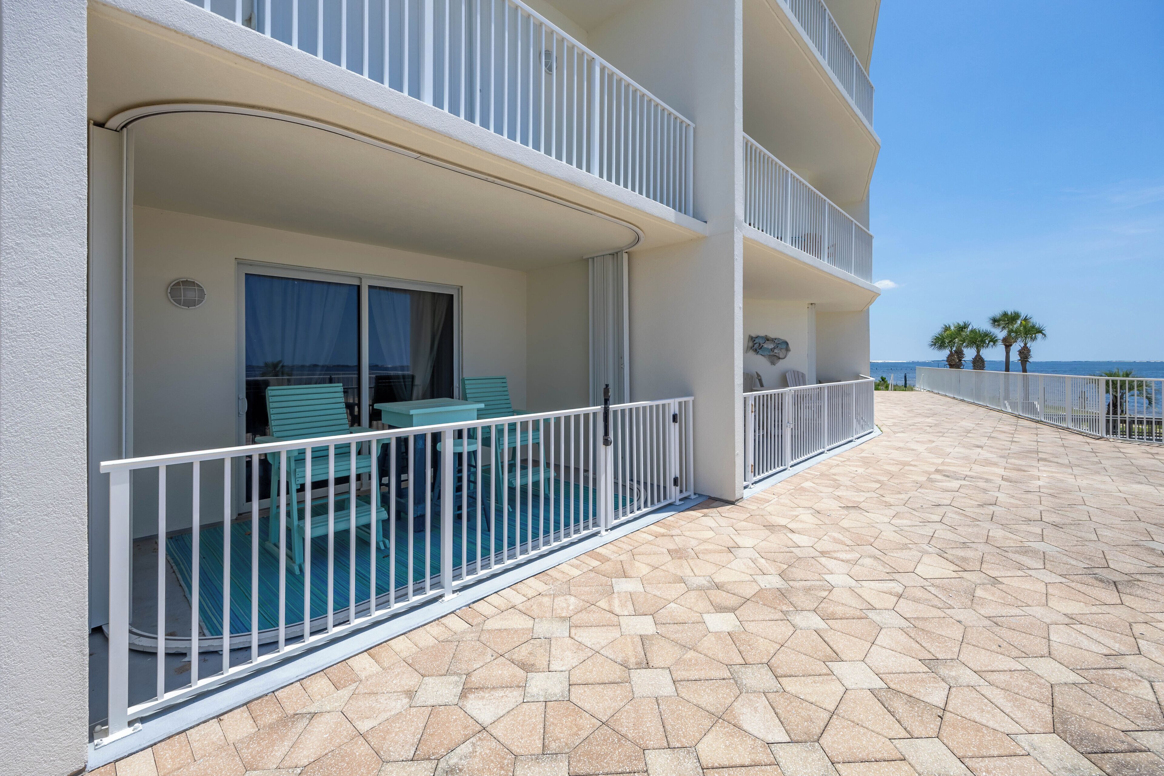 A hotel balcony with a pool, outdoor seating, and a view of the ocean.