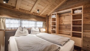 Une chambre dans un chalet en bois, comprenant un lit, des tables de chevet, une fenêtre avec des rideaux et une étagère intégrée en bois.