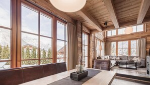 A wooden interior with large windows, a sofa, and a dining table. - Modern Chalet in the Willow Roof (Leutasch)