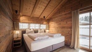 A wooden cabin bedroom with a bed, bedside lamps, and a window with curtains. - Modern Chalet in the Willow Roof (Leutasch)