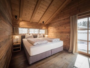 Un dormitorio de cabaña de madera con cama, lámparas de noche y una ventana con cortinas.