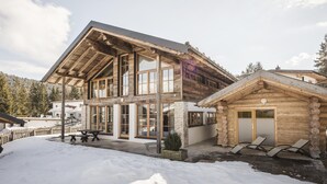 Une cabane en rondins dotée d’un grand porche, d’une dépendance en bois séparée et d’une cour enneigée.