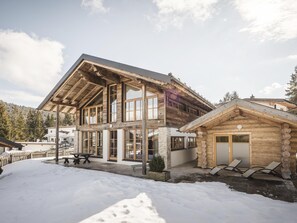 A log cabin with a large porch, a separate wooden structure, and a snow-covered yard. - Modern Chalet in the Willow Roof (Leutasch)