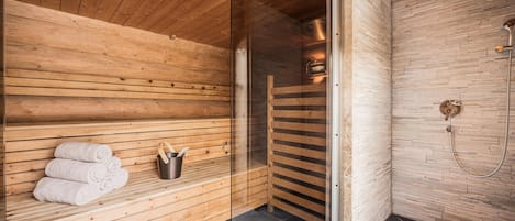 A sauna with wooden benches, a glass door, and a shower area with a tiled floor.