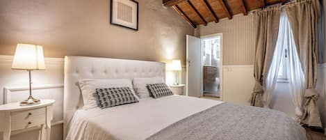 Un dormitorio con una cama grande, dos mesitas de noche, un ventilador de techo y una ventana con cortinas.
