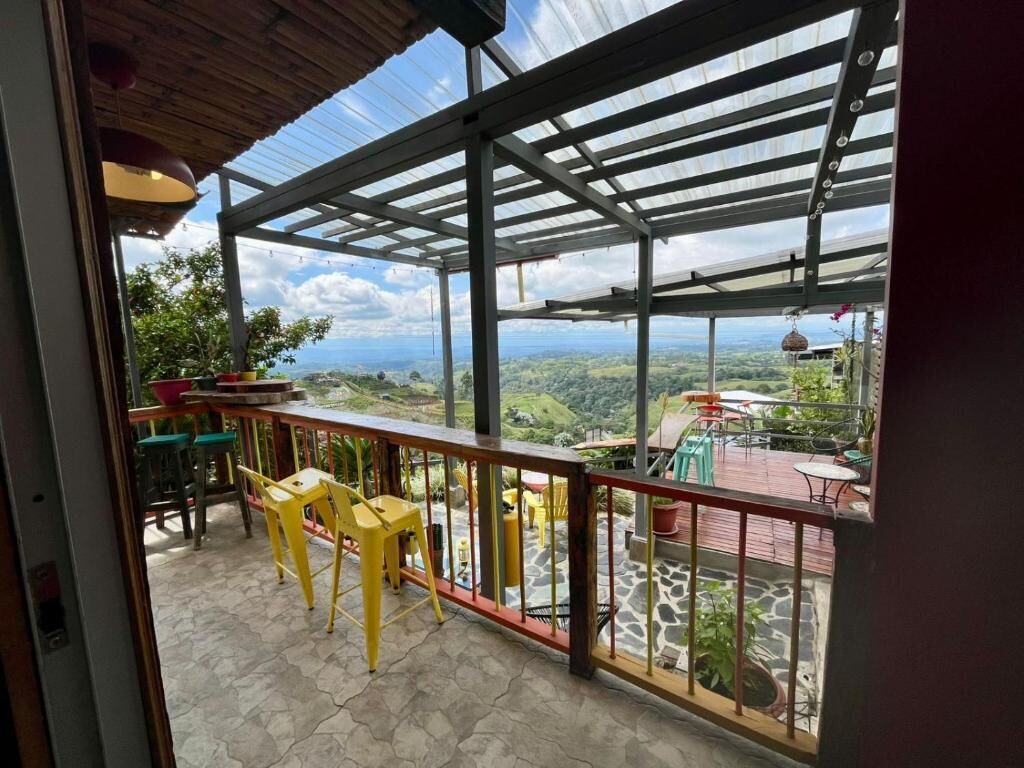 A balcony with a view of the landscape, a table, chairs, and a railing.