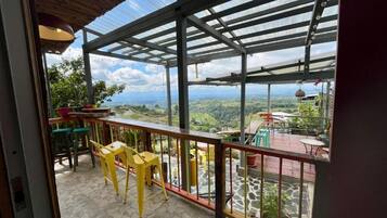 A balcony with a view of the landscape, a table, chairs, and a railing.