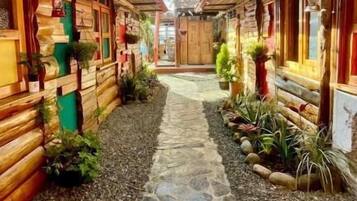 Un estrecho sendero de piedra bordeado por edificios de madera con plantas en macetas y luces colgantes.
