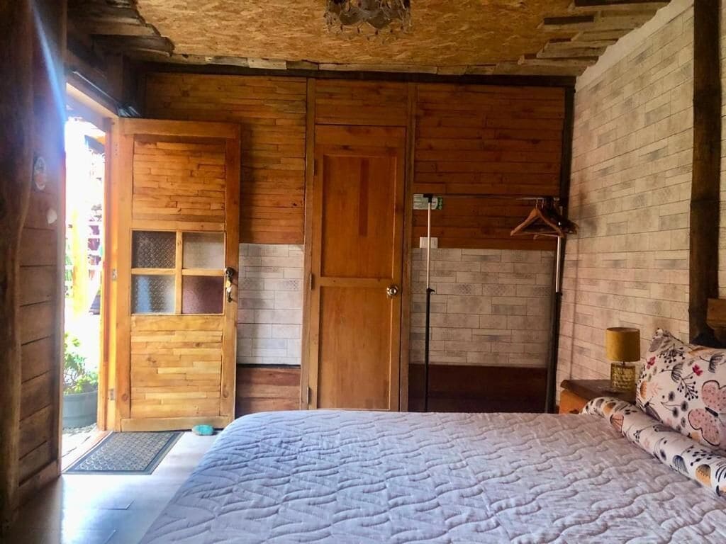 A wooden room with a bed, a wardrobe, and a door leading outside.