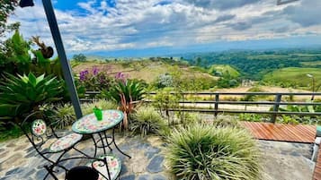 Um pátio com piso de pedra, uma mesa redonda com cadeiras e vista para colinas verdes.