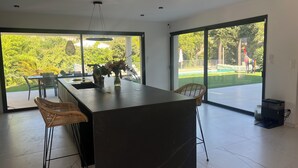 A modern kitchen with a large island, two bar stools, and a vase of flowers. - Exceptional home with a pool (La Seyne-sur-Mer)