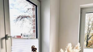 Ein Zimmer mit Fenster, einer Flasche und einer Vase mit Trockenblumen.
