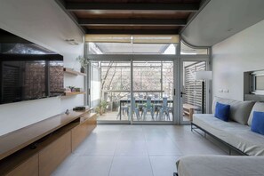 A modern living room with a flat-screen TV, a sofa with blue cushions, a dining area with chairs, and a sliding glass door leading to an outdoor space. - MOT Rentals + Concepcion Hotel - 3 Bd 2 Ba Parking, Gym and Pool (Buenos Aires)