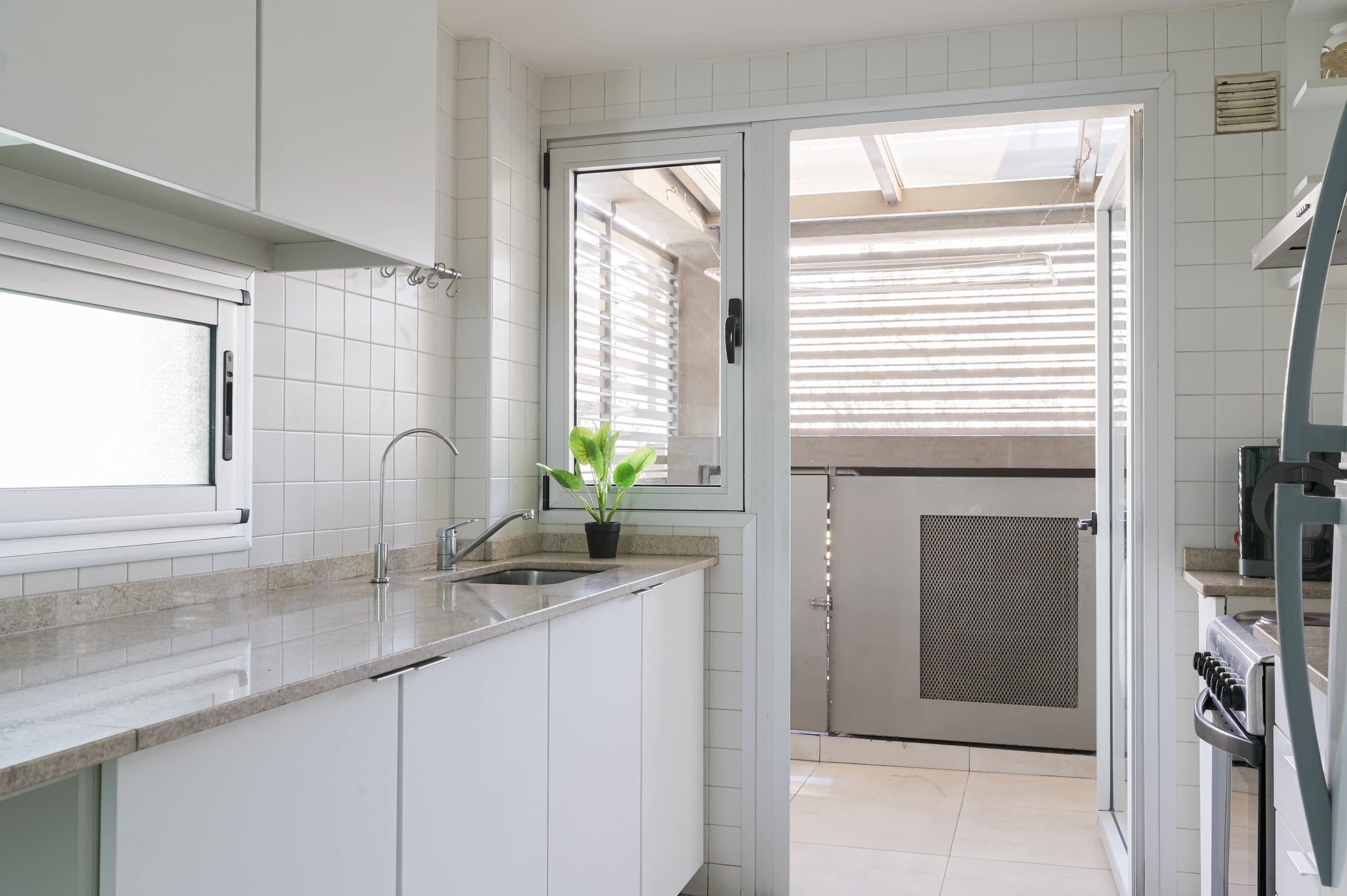 A modern kitchen with white cabinets, a sink, a potted plant, and a sliding glass door leading to a balcony.