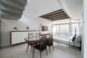 A modern dining area with a glass table, wooden chairs, a sofa, and a staircase. - MOT Rentals + Concepcion Hotel - 3 Bd 2 Ba Parking, Gym and Pool (Buenos Aires)
