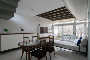 A modern dining area with a glass table and wooden chairs, a built-in bench, and a large window with a view of the outdoors. - MOT Rentals + Concepcion Hotel - 3 Bd 2 Ba Parking, Gym and Pool (Buenos Aires)