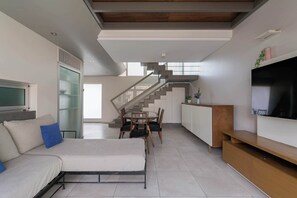 A modern living room with a sofa, a bed, a dining area with chairs, a staircase, and a TV. - MOT Rentals + Concepcion Hotel - 3 Bd 2 Ba Parking, Gym and Pool (Buenos Aires)
