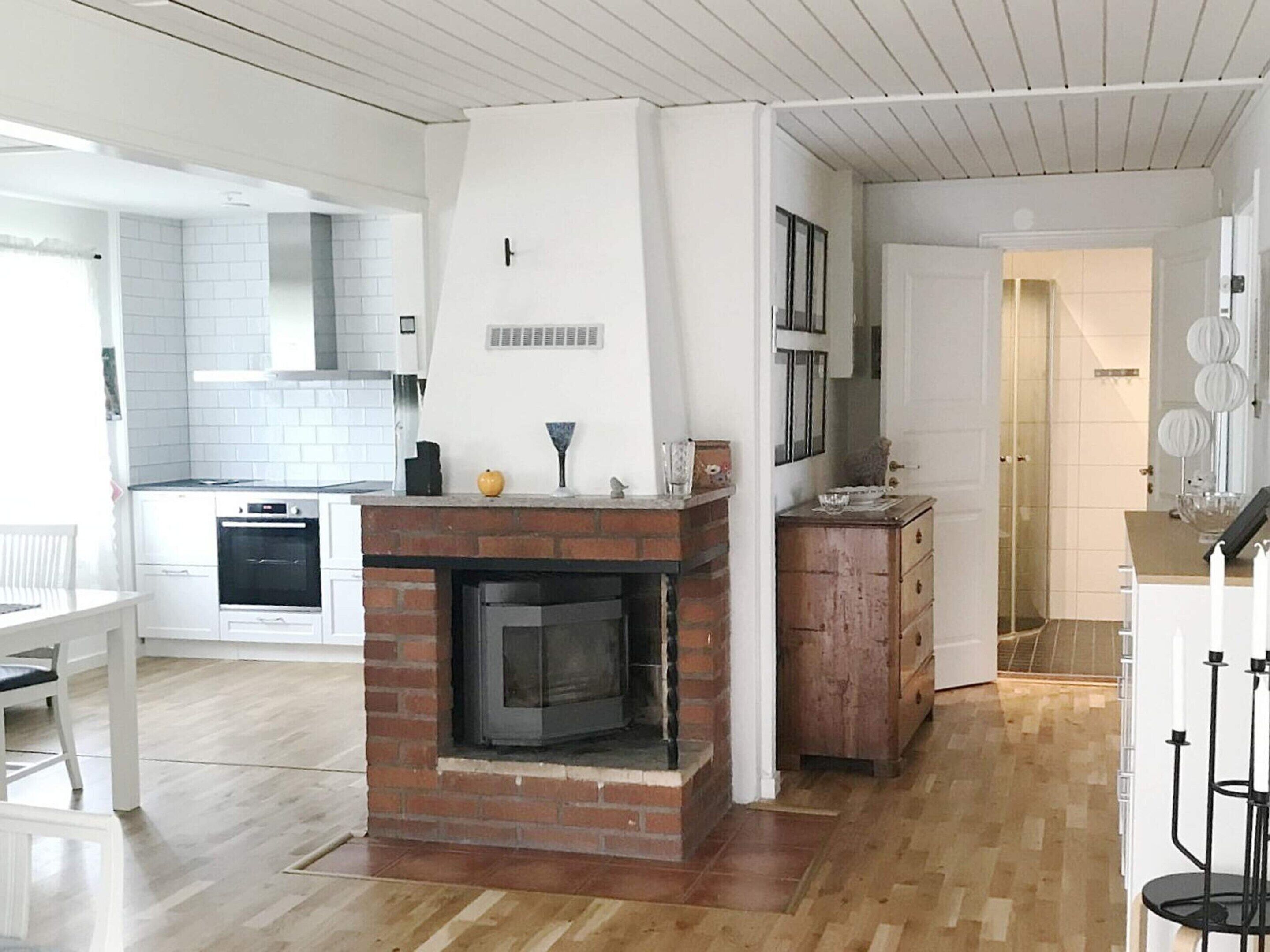 Una cocina moderna con chimenea de ladrillo, armarios blancos y un comedor con mesa y sillas blancas.