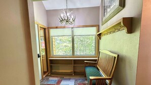 A corner room with a bench, a window with blinds, a chandelier, and a patterned rug.