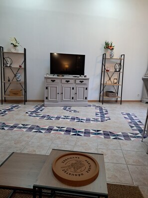 Una sala de estar con televisor, armarios blancos, piso estampado y una mesa con posavasos.