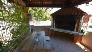 An outdoor patio with a wooden table and benches, a brick oven, and a metal fence. - Apartments Snjezana Carev - Studio Apartment With Balcony (Tisno)