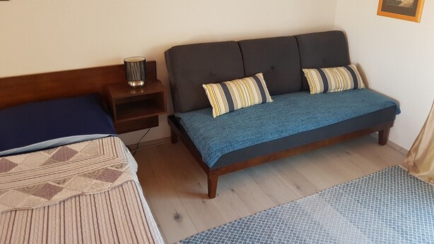 A bedroom with a bed, a sofa, a nightstand, and a lamp. - Apartments Snjezana Carev - Studio Apartment With Balcony (Tisno)