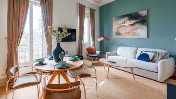 Uma sala de estar moderna com um sofá branco, uma mesa de jantar com cadeiras, um vaso com flores e um quadro na parede.