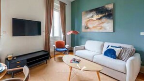 Uma sala de estar com televisão de tela plana, um sofá, uma mesa de centro e um quadro na parede.