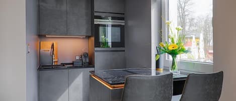 Una cocina moderna con armarios grises, horno empotrado y comedor con dos sillas.