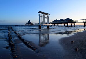 A pier extending into the water with a structure at the end, a sandy beach, and a calm sea. - Appartement mit Pool in Heringsdorf (Heringsdorf)